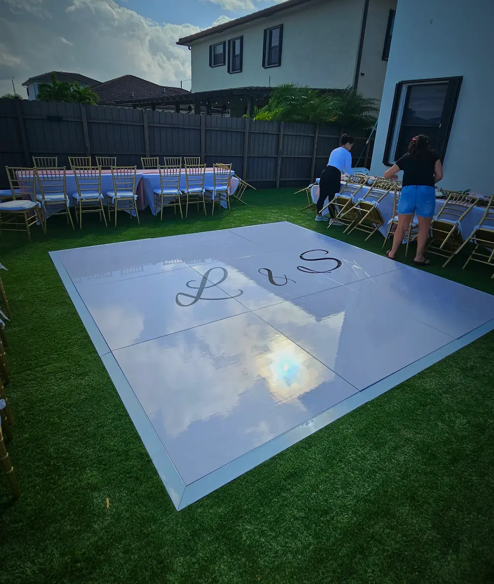 Glossy white wedding dance floor with L and S initials installed on artificial turf in a Miami backyard
