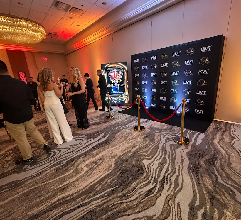 Guests near a vertical LED screen and branded backdrop with amber blue and white corporate uplighting in Miami