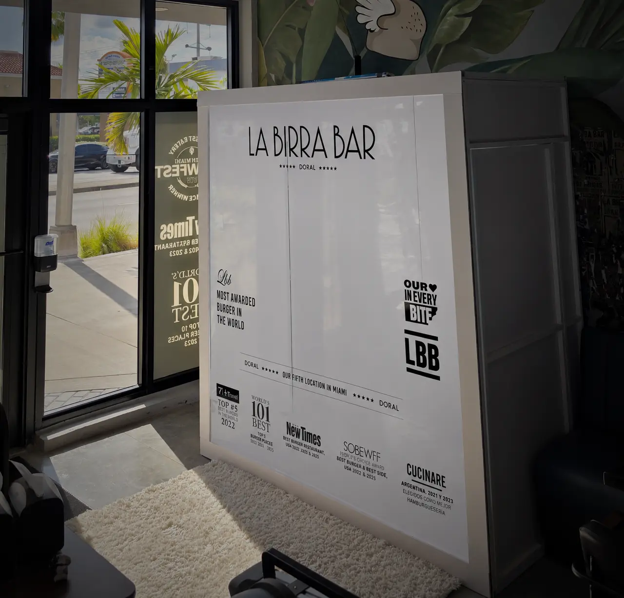 Side view of the branded magazine box photo booth just inside La Birra Bar’s glass entrance in Doral