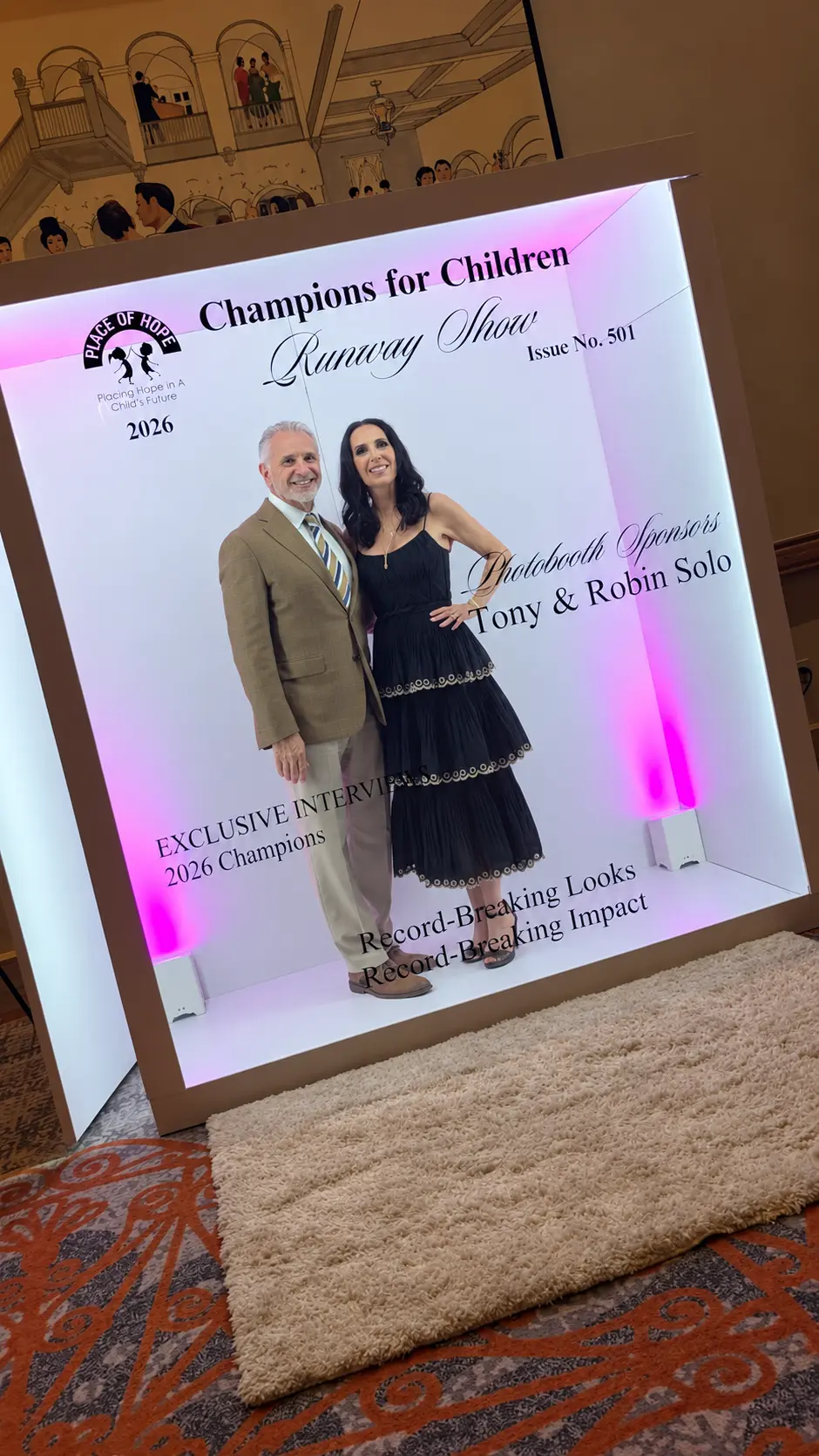 Two guests posing inside the Champions for Children magazine cover booth in Boca Raton