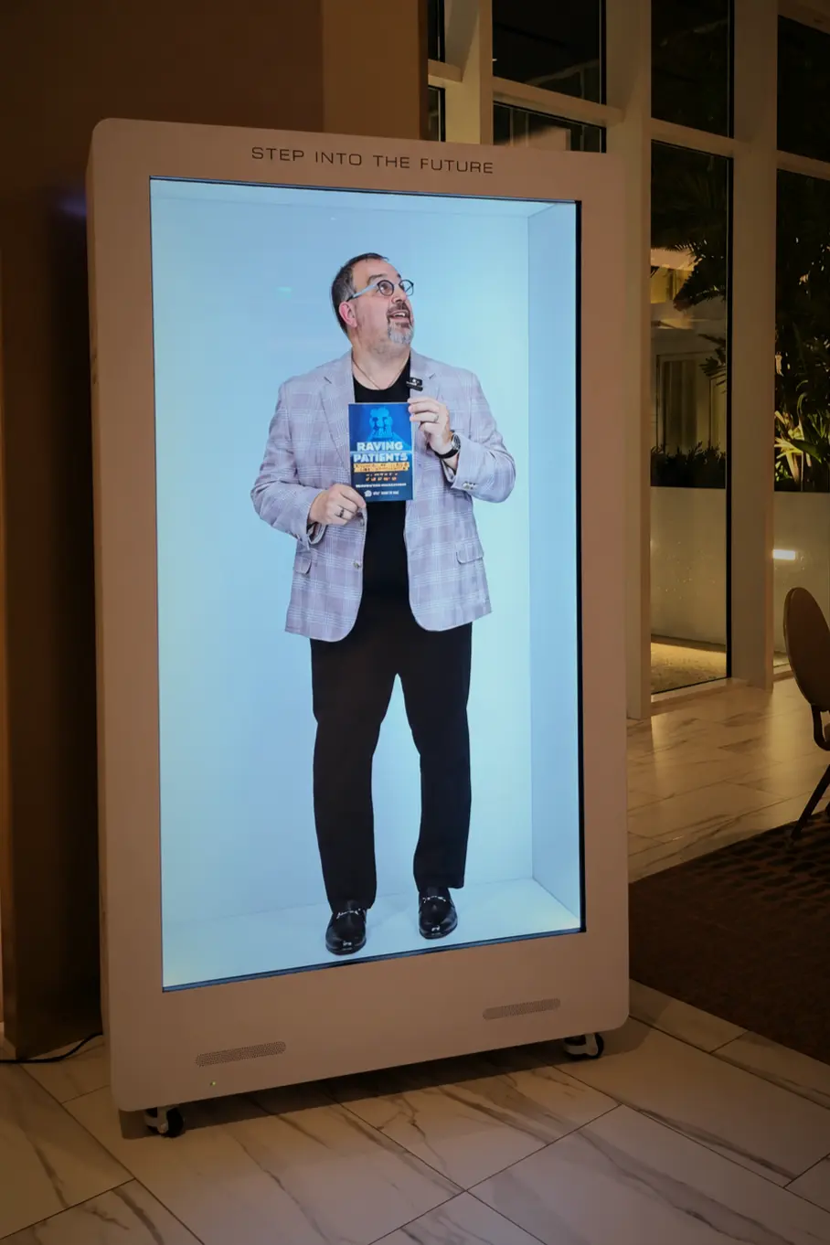 Dr. Len Tau holding Raving Patients Supercharged inside the life-size hologram display at Pier Sixty-Six