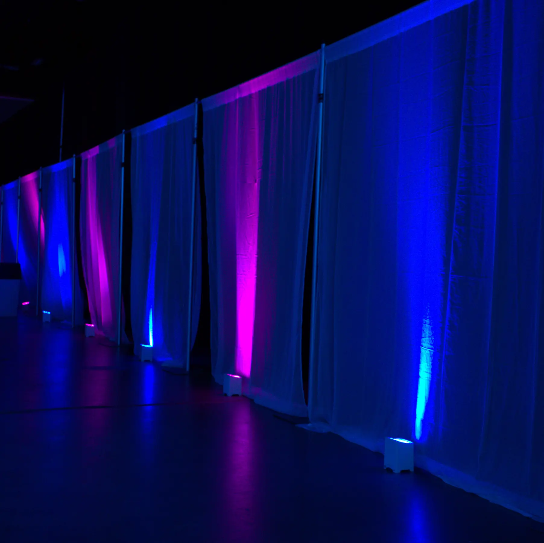 Blue and magenta wireless uplighting washing a row of event draping